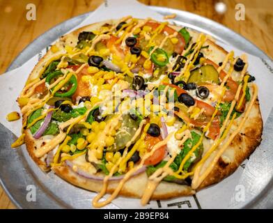 Pizza mit schwarzen Oliven, jalapeños, Spinat, goldenem Mais, Pickeln, Zwiebeln und Tomaten Stockfoto