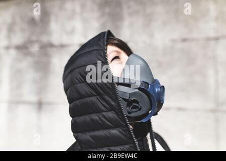 Frau mit Gasmaske auf der Straße, die auf den Himmel blickt und auf die Luft wartet, um wieder sauber und koronavirusfrei zu werden Stockfoto