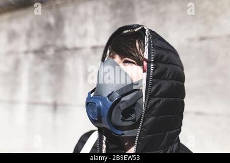 Frau mit Gasmaske auf der Straße, die auf den Himmel blickt und auf die Luft wartet, um wieder sauber und koronavirusfrei zu werden Stockfoto