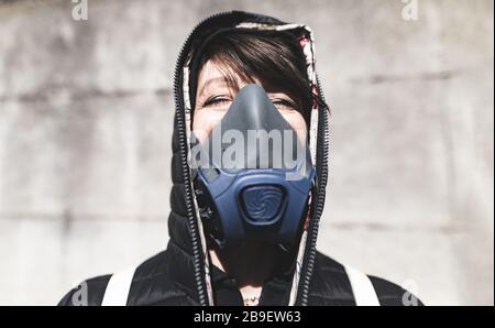 Frau mit Gasmaske auf der Straße, die auf den Himmel blickt und auf die Luft wartet, um wieder sauber und koronavirusfrei zu werden Stockfoto