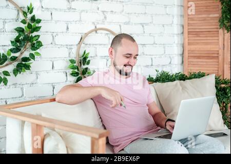 Auf dem Sofa sitzt ein Mann mit einem Laptop auf dem Schoß Stockfoto
