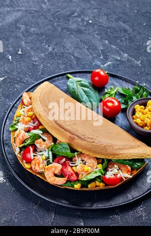 Der Restaurantteil des klassischen asiatischen Dickpfannkuchens mit Garnelen, Spinatblättern, Mais, Kirschtomaten, zerfetztem Weißkäse auf einem schwarzen Teller auf einem Stockfoto