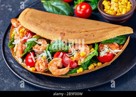 Singapur Dickpfannkuchen mit Garnelen, Spinatblättern, Mais, Kirschtomaten, geschredderten Weißkäse auf einer schwarzen Platte mit Ketchup und Petersilie auf einer dunklen Stockfoto