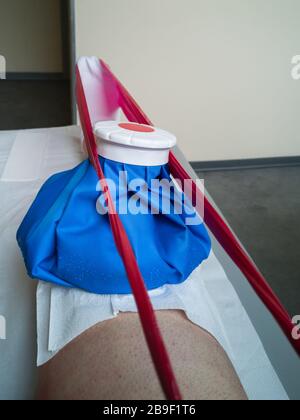 Rehabilitation mit elastischem roten Band und Eis am Knie auf dem Physiotherapiebett in einem medizinischen Zentrum. Stockfoto