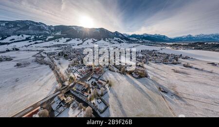 Luftbild der kleinen gemütlichen deutschen Stadt am Berggrund bei Sonnenaufgang in einer Wintersaison sind Halblechstadt, Deutschland, Bayern, Baumzweige Stockfoto