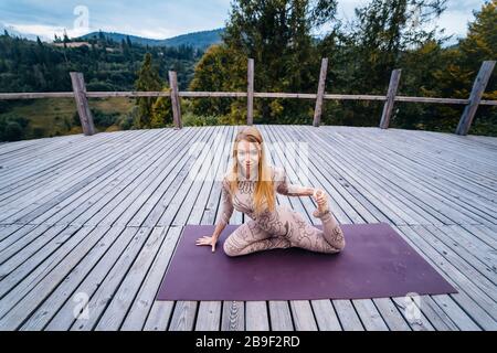 Eine Frau übt am Morgen auf einer Terrasse an frischer Luft Yoga. Stockfoto