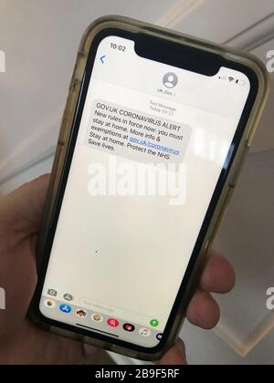Ein Mann hält das Handy mit einer SMS-Warnung, die von der Regierung gesendet wurde und warnt, dass neue Regeln in ganz Großbritannien in Kraft sind und die Menschen zu Hause bleiben müssen. Die Nachricht wurde am Morgen gesendet, nachdem Premierminister Boris Johnson das Vereinigte Königreich in Sperrstellung versetzt hatte, um die Ausbreitung des Coronavirus einzudämmen. Stockfoto