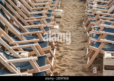 Zwei gegensätzliche Reihen von schwebenden leeren Liegen in Reihen reihten sich in Ordnung am Strand im Sand, zwei gegenüberliegende Reihen von aufgerichteten l Stockfoto