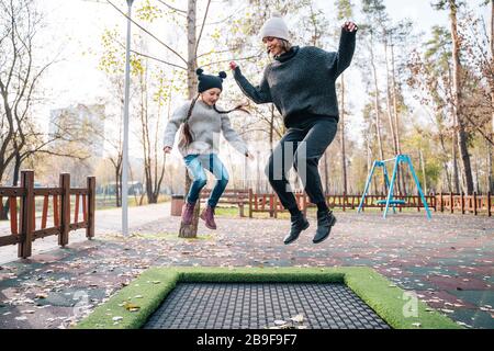 Im Herbstpark springen Mutter und Tochter zusammen auf Trampolin Stockfoto