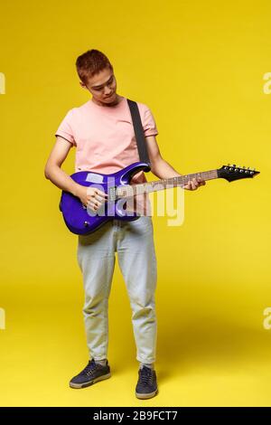 Voller Länge hübsche junge Musiker, die Gitarre spielen und singen, isoliert auf gelbem Hintergrund