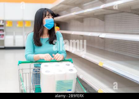 Asian Woman betrachtet leere toilettenpapierregale im Supermarkt inmitten der COVID-19-Coronavirus Ängste, Käufer panischen Kauf und Lagerung von toilettenpapier Vorbereitung Stockfoto