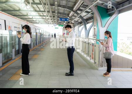 Drei Asiaten, die einen Meter von anderen Menschen entfernt mit einer Maske stehen, halten Abstand vor COVID-19-Viren und sozialen Distancin Stockfoto
