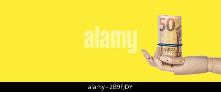 Holzhand mit Geld isoliert auf gelbem Hintergrund. Euro-Banknoten rollten in eine Röhre. 50-Euro-Scheine mit Platz für Kopien. Langes, breites Banner. Cop Stockfoto