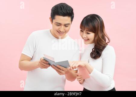 Glücklicher asiatischer Mann und Frau, der Pässe und Flugtickets hält, während er die auf Pink isolierte Kamera betrachtet Stockfoto