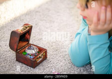 Nahaufnahme des fünfjährigen Jungen, der eine Schatzkiste voller bunter Schmucksteine bewundert. Er hat Edelsteine auf dem Boden aufgereiht. Stockfoto