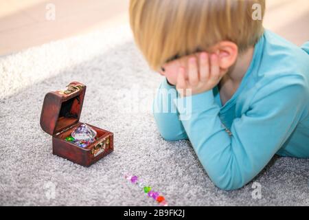 Fünf Jahre alter Junge, der eine Schatzkiste voller bunter Juwelen bewundert. Er hat Edelsteine auf dem Boden aufgereiht. Stockfoto