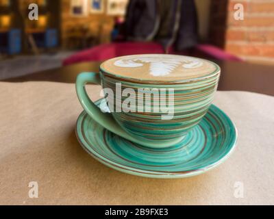 Eine Tasse Cappuccino steht auf einem Tisch in der Cafeteria auf einem Blatt Handwerkspapier. Stockfoto