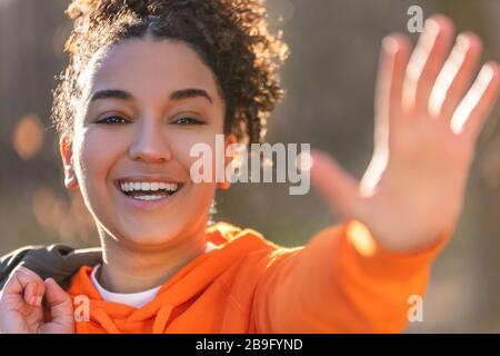 Outdoor-Porträt der schönen glücklichen gemischten Rasse afroamerikanische Mädchen Teenager junge Frau lachend, winkend und lächelnd mit perfekten Zähnen in Go Stockfoto