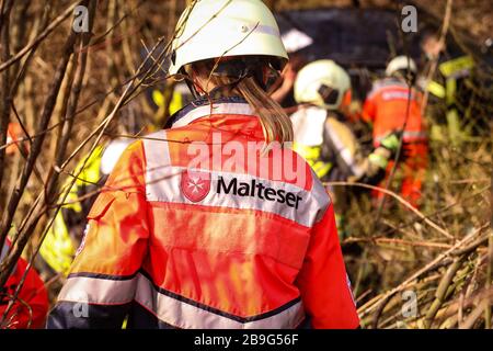 19. März 2020, Sachsen, Wilsdruff: Maltesischer Sanitäter mit Helm auf dem Weg zur Unfallstelle in unwegsamem Gelände. Im verschwommenen Bildhintergrund sind Rettungskräfte und ein Unfallwagen Foto: Tino Plunert / dpa-Zentralbild / ZB Stockfoto