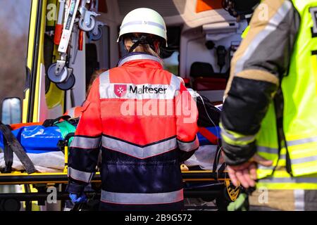 19. März 2020, Sachsen, Wilsdruff: Im Zentrum des Bildes steht der Sanitäter der Malteser International bei einem offenen Rettungswagen. Sanitäter tragen einen Helm und Schutzhandschuhe. Im Hintergrund des Bildes steht ein offener Rettungswagen. Davor ein Rettungstisch. Im verschwommenen Vordergrund steht ein Feuerwehrmann in der Sektion Foto: Tino Plunert / dpa-Zentralbild / ZB Stockfoto