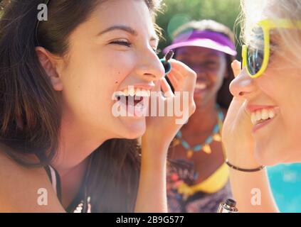 Fröhliche Teenager-Freundinnen, die Mascara auf einer sonnigen Terrasse auftragen Stockfoto