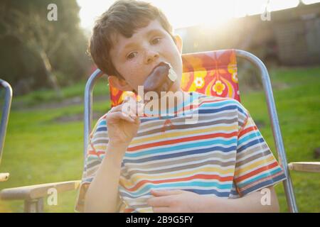 Portrait Junge essen Schokoladeneis Bar auf der Sommerterrasse Stockfoto