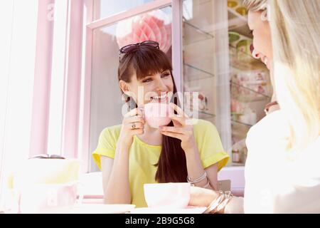 Fröhliche junge Frauen Freunde trinken Kaffee im sonnigen Café Stockfoto