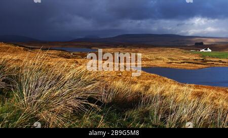 Irische Landschaft mit Grasfeldern, See und einem entfernten Ferienhaus, dunkle Wolken und schlechtes Wetter kommen schnell über die Berge von Connemara Irland Stockfoto