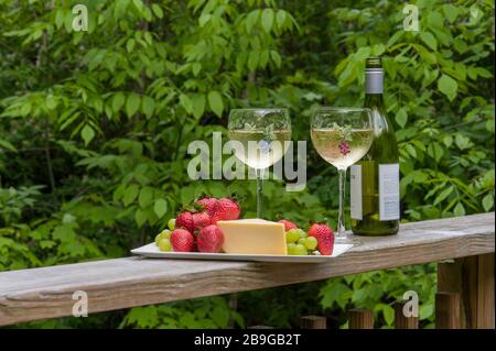 Kleine Platte mit Käse und Obst und zwei Weingöschen auf dem Decksgeländer. Stockfoto