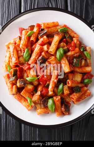 Vegetarische Tortiglioni Pasta mit Gemüse und Basilikum in Tomatensauce in einem Teller auf dem Tisch. Vertikale Draufsicht von oben Stockfoto