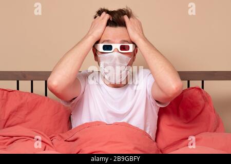 Junger kaukasischer Mann sieht Horror-Film zuhause im Bett in einer 3D-Brille, die die Hände am Kopf hält. Studio gedreht Stockfoto