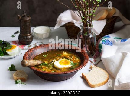 Frühlingsgrüne Suppe mit Kräutern, Gemüse und grünen Erbsen, serviert mit Ei und Sauerrahm. Rustikaler Stil. Stockfoto