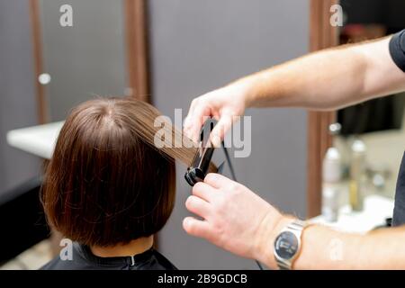 Friseursalon glättet die Haare der Frau mit Haarglättwerkzeug im Friseursalon. Stockfoto