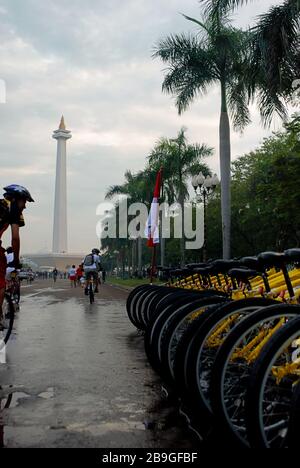 Radfahrer, die parkte Fahrräder mit Nationaldenkmal im Hintergrund passieren. Jakarta, Indonesien. Stockfoto