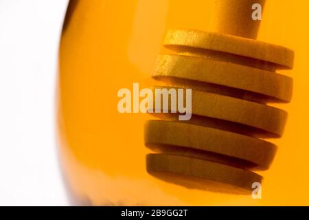 Ein hölzerner Honigtriesler tauchte in ein Glas klaren Honigs zurück beleuchtet durch goldenes transparentes Licht. Stockfoto