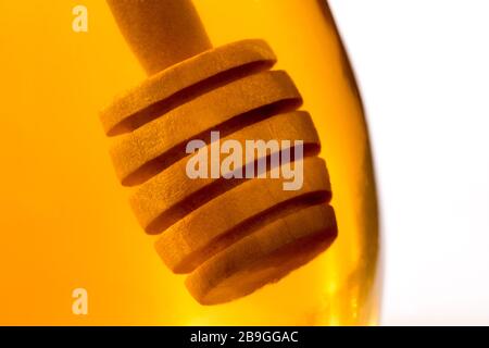 Ein hölzerner Honigtriesler tauchte in ein Glas klaren Honigs zurück beleuchtet durch goldenes transparentes Licht. Stockfoto