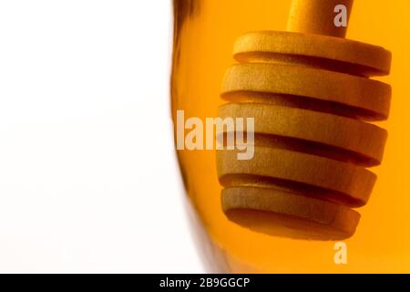 Ein hölzerner Honigtriesler tauchte in ein Glas klaren Honigs zurück beleuchtet durch goldenes transparentes Licht. Stockfoto