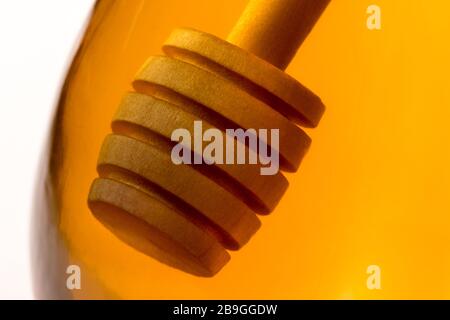 Ein hölzerner Honigtriesler tauchte in ein Glas klaren Honigs zurück beleuchtet durch goldenes transparentes Licht. Stockfoto