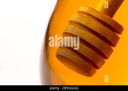 Ein hölzerner Honigtriesler tauchte in ein Glas klaren Honigs zurück beleuchtet durch goldenes transparentes Licht. Stockfoto