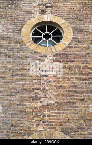 Alte Mauer aus Backstein und Rundfenster auf einem neu beengten Lagerhaus in der Insel der Hunde in der Regenerationsregion Docklands in London. Stockfoto