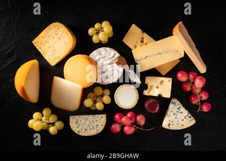 Käse, viele verschiedene Arten, von oben auf schwarzem Grund mit Trauben geschossen Stockfoto