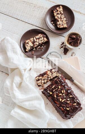 Hausgemachter Kuchen ohne Backe mit Schokoladenbiskuit auf einem weißen Holztisch. Fauliger Kuchen oder Mosaikkuchen oder Schokoladensalami flacher Laienstil Stockfoto