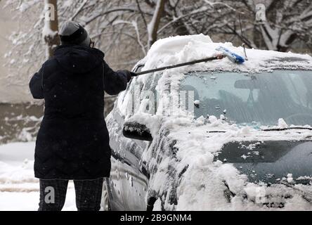 Frau säubert ein Auto aus schwerem Schnee. Stockfoto