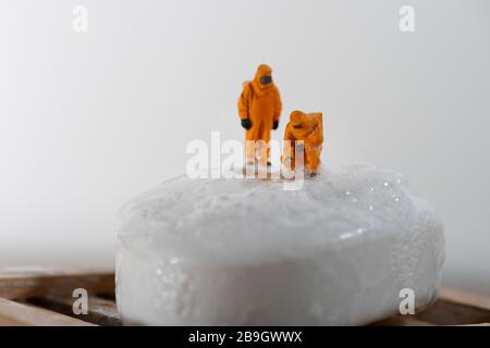 Konzeptbild für Coronavirus mit Miniaturmenschen auf einer Seifenleiste in Haselmatt-Anzügen, die auf Bakterien getestet werden. Stockfoto