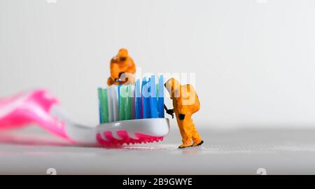 Ein Konzeptbild für Coronavirus, das Tests auf Bakterien auf einer Zahnbürste mit Miniaturmenschen in einem Hazmat-Anzug zeigt. Stockfoto