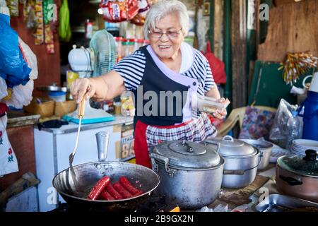 Frau, die Würstchen in einer Bratpfanne auf den Straßen des öffentlichen Carbon-Marktes kocht. Stockfoto