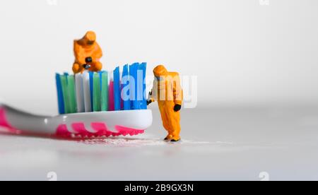 Ein Konzeptbild für Coronavirus, das Tests auf Bakterien auf einer Zahnbürste mit Miniaturmenschen in einem Hazmat-Anzug zeigt. Stockfoto