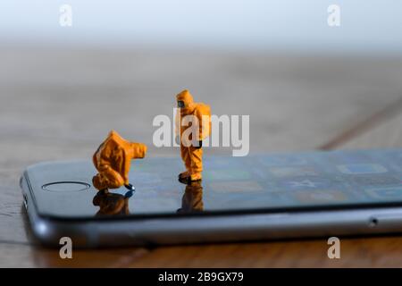 Ein Konzeptbild zur Demonstration der Verbreitung von Coronavirus mit Miniaturfiguren, die auf Bakterien auf einem Mobiltelefon getestet wurden Stockfoto