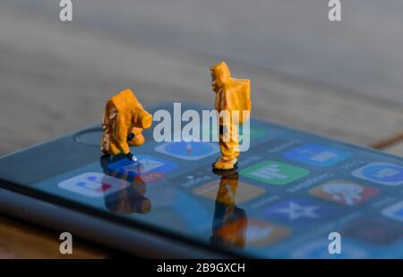 Ein Konzeptbild zur Demonstration der Verbreitung von Coronavirus mit Miniaturfiguren, die auf Bakterien auf einem Mobiltelefon getestet wurden Stockfoto