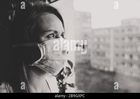 Frau in medizinischer Maske in der Nähe des Fensters. Quarantäne zu Hause. Stockfoto